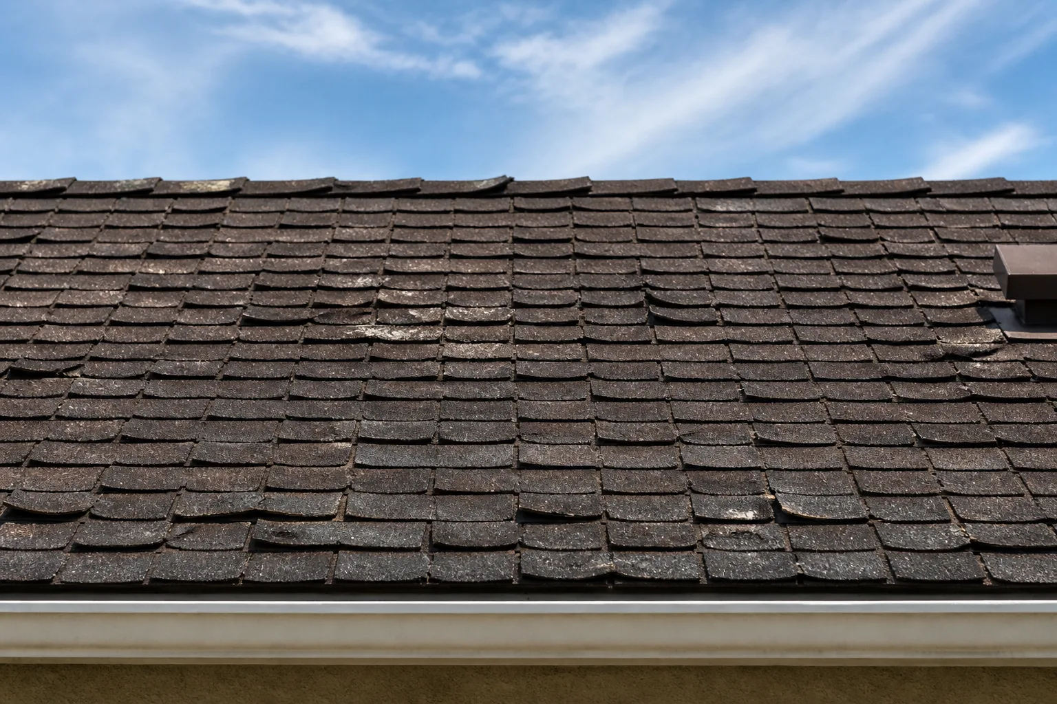 Residential roof section with aged asphalt shingles showing wear and curling.