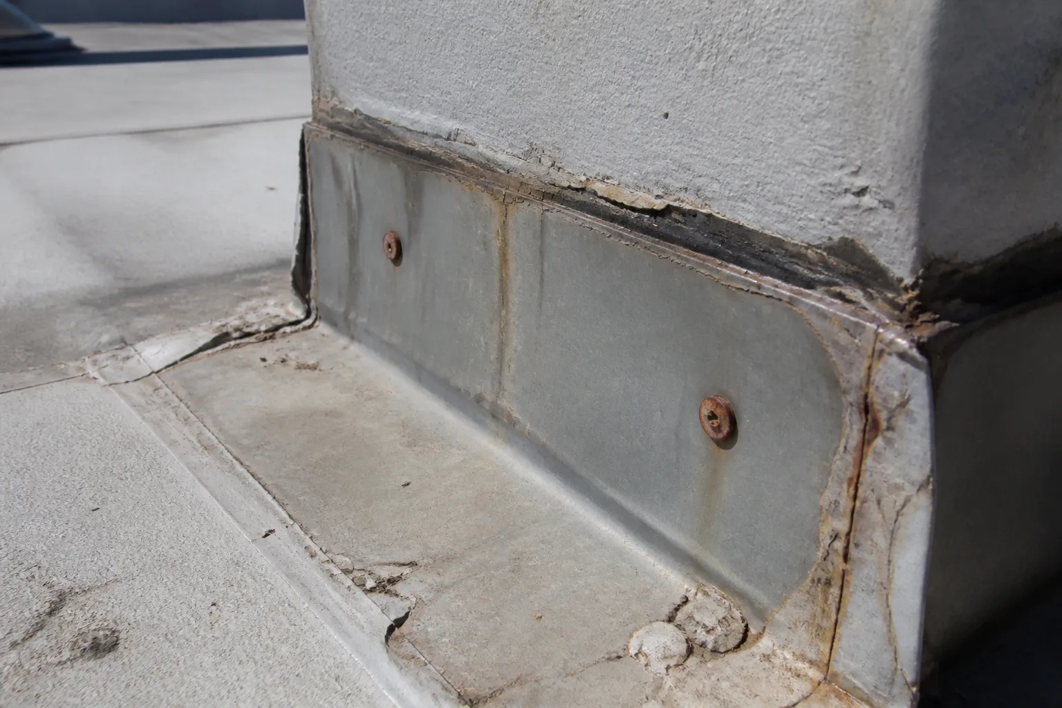 Close-up of roof flashings and penetrations with visible wear on a sunny rooftop.